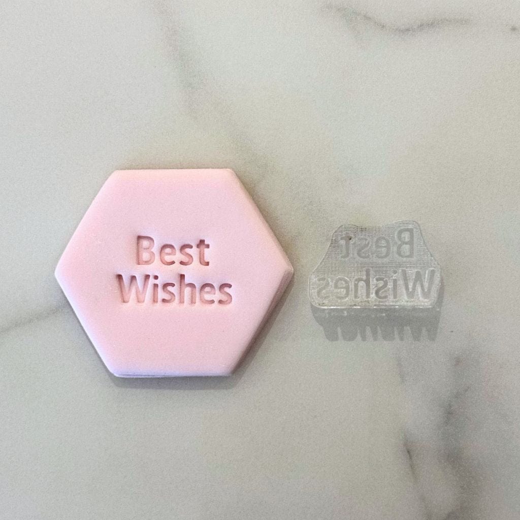 Pink fondant cookie stamped with Best Wishes and acrylic stamp beside it