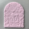 Arched fondant cookie embossed with a reindeer surrounded by festive designs using an acrylic embosser stamp