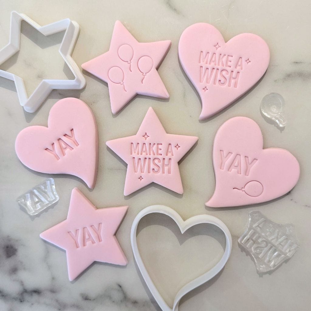Pink fondant cookies stamped with YAY and Make a Wish, alongside cutters