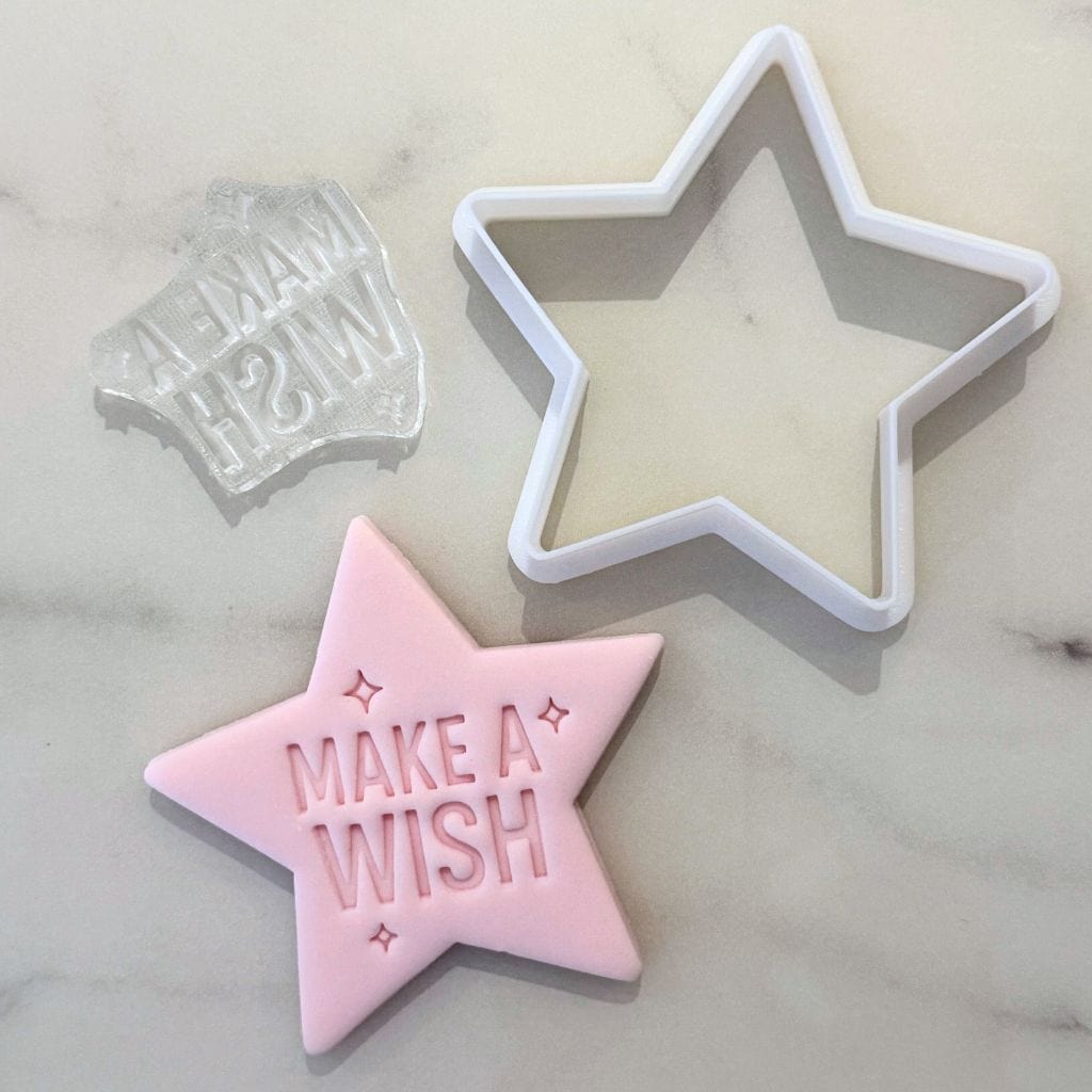 Star cookie cutter with fondant and Make a Wish stamp on marble surface.