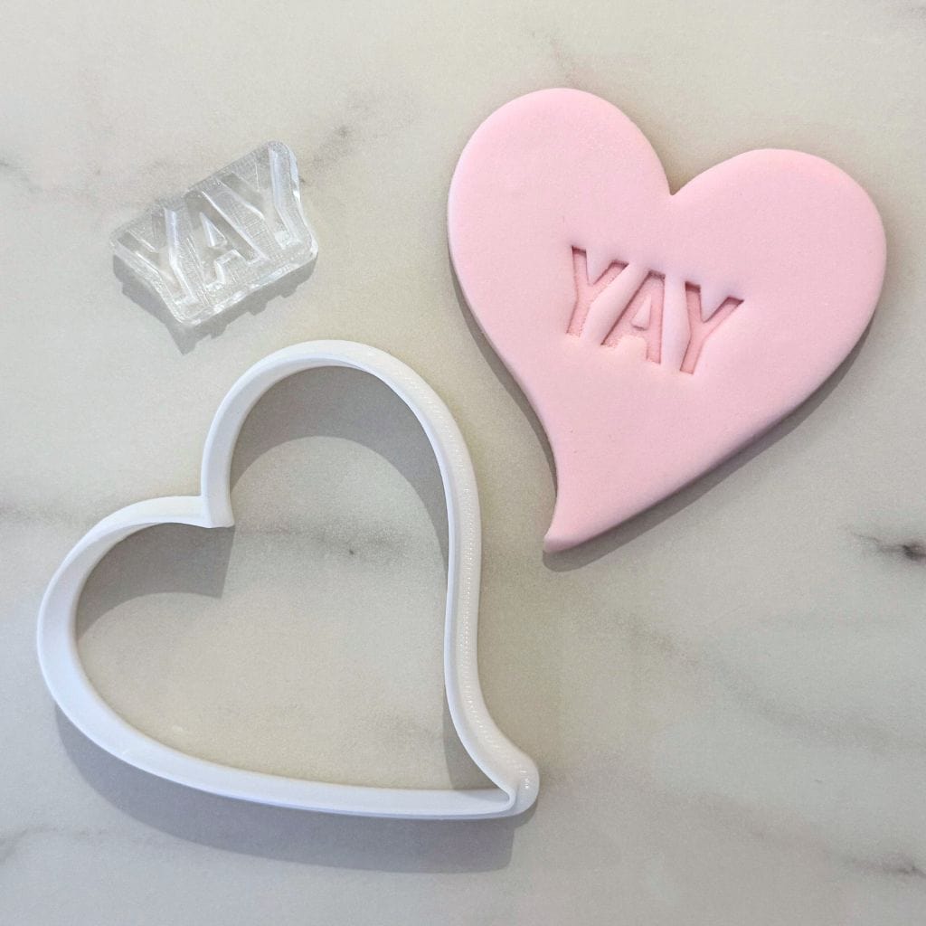 Heart cookie cutter with mini YAY fondant stamp on pink cookie.