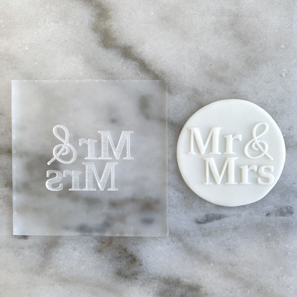 Custom acrylic embosser stamp beside a cookie decorated with "Mr. & Mrs." in raised fondant.